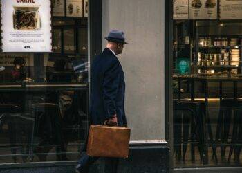 man in black suit jacket and blue hat standing in front of store
