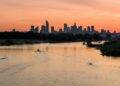 A boat traveling down a river with a city skyline in the background